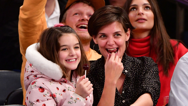 Suri Noelle and Katie Holmes smiling while sharing a bite courtside