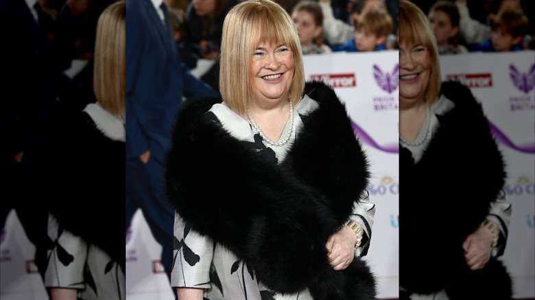 Susan Boyle on the red carpet wearing a black fur stole and a pearl necklace.