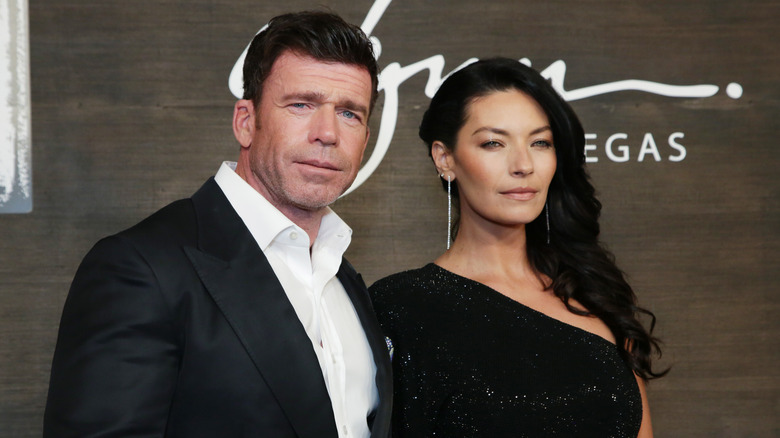 Taylor Sheridan and wife Nicole Muirbrook posing on the red carpet in a black coat and sparkly black gown, respectively.