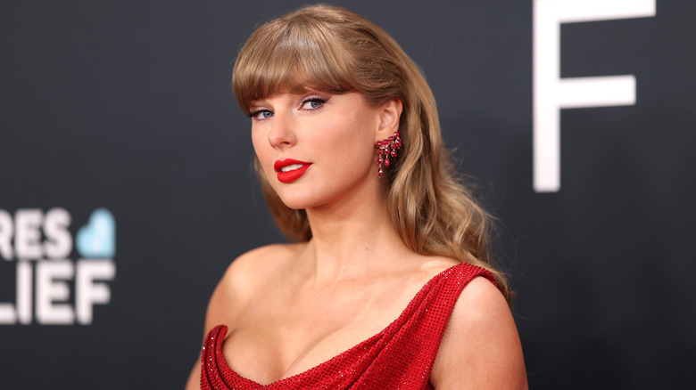 Taylor Swift in a red dress stands on the red carpet