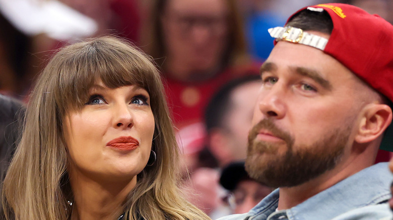 Taylor Swift sitting with Travis Kelce and looking upward.