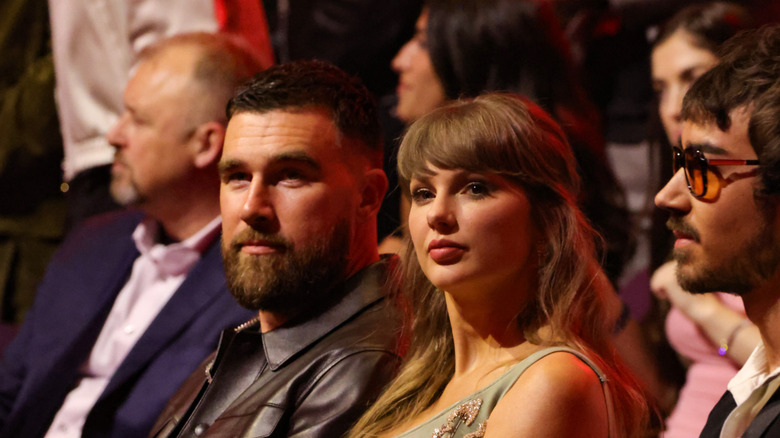 Travis Kelce and Taylor Swift looking sideways while sitting together at an event