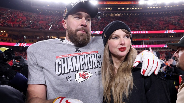 Travis Kelce wraps his arm around Taylor Swift as they look away from the camera.