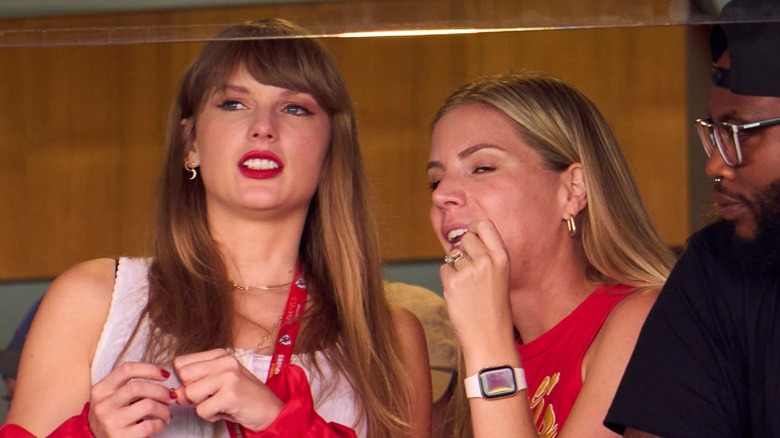 Taylor Swift leans toward a friend while clenching her fist and grinning her teeth during a game.