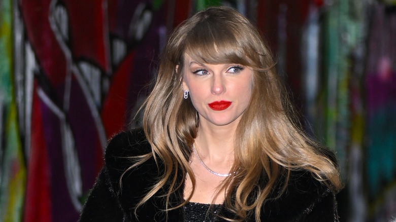 Sporting bright red lipstick and a black fur coat, Taylor Swift looks away from the camera.