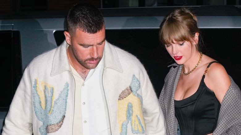 Travis Kelce and Taylor Swift gaze downward while stepping away from a car.