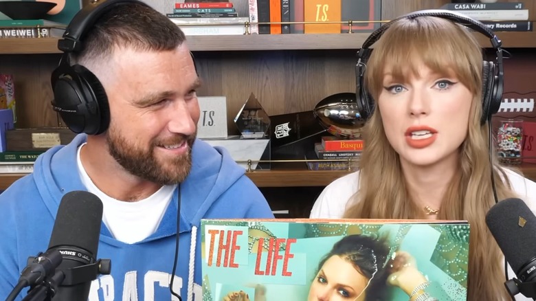 Travis Kelce gazes at Taylor Swift, who's holding a vinyl copy of her album.