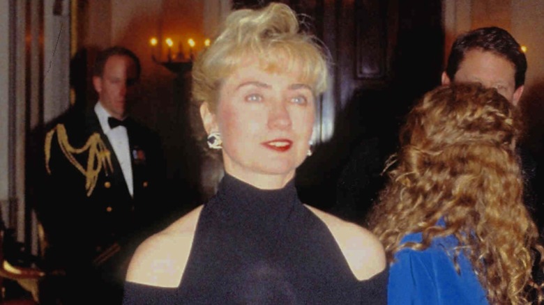 Wearing red lipstick and a navy dress with shoulder cutouts, Hillary Clinton looks away from the camera