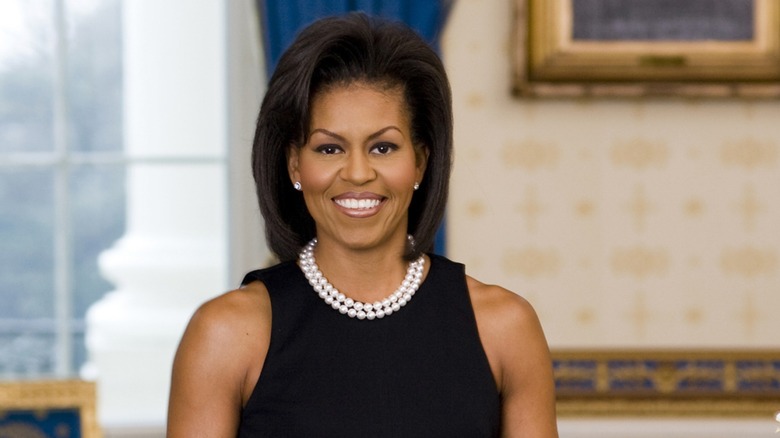 Dressed in a sleeveless black dress that shows her bare arms, Michelle Obama smiles at the camera