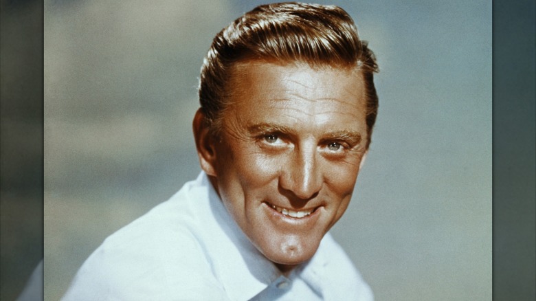 Kirk Douglas pictured smiling and wearing a white collared shirt in a close-up.