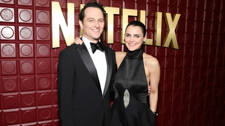 Kerri Russell wearing a black dress with a silver eye-shaped detail and posing with her arm around Matthew Rhys