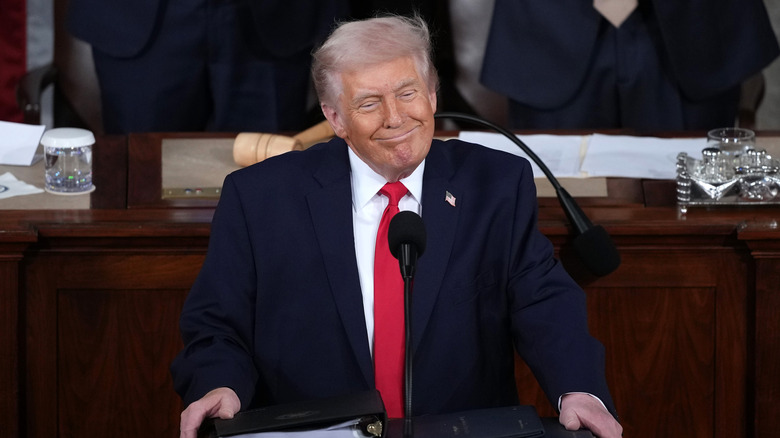 Donald Trump smiling while giving his 2026 State of the Union address in a black suit with a red tie