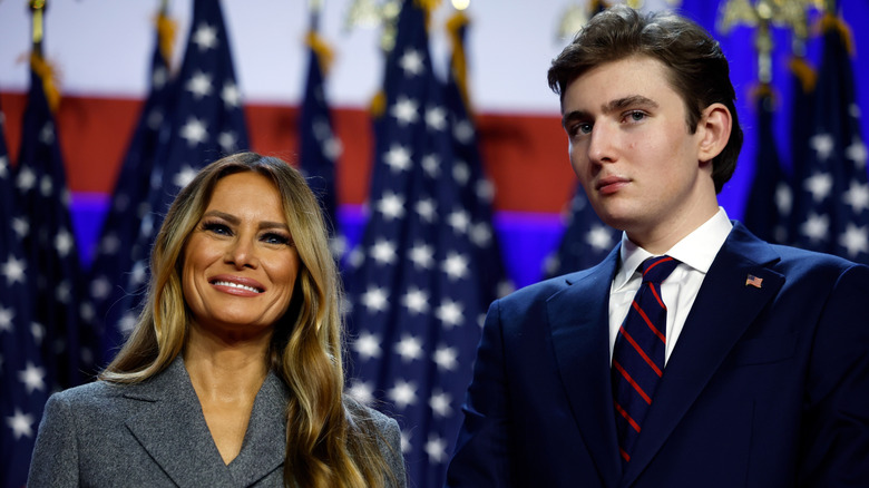 Melania Trump and Barron Trump smiling in front of American flags on 2024 election night at the Palm Beach Convention Center