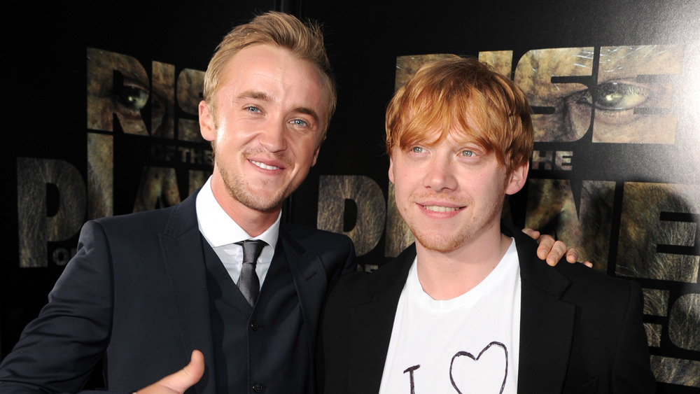 Tom Felton and Rupert Grint smiling while posing arm in arm at a movie premiere
