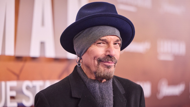 Billy Bob Thornton mischievously grinning in a blue fedora and gray beanie.