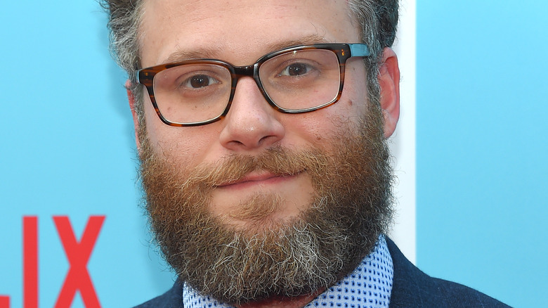 Seth Rogen poses in a suit and tie with glasses.