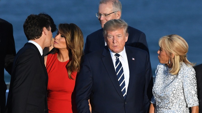 Melania Trump makes a kissing face toward Justin Trudeau behind Donald Trump, as Brigitte Macron looks on.