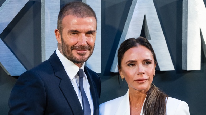 David Beckham smiles while leaning toward a stone-faced Victoria Beckham.