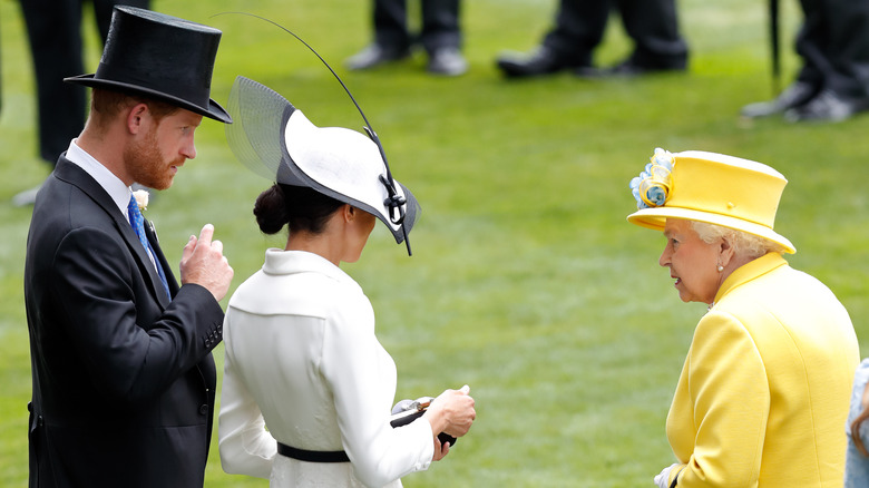 Queen Elizabeth, Meghan Markle, and Prince Harry standing next to each other