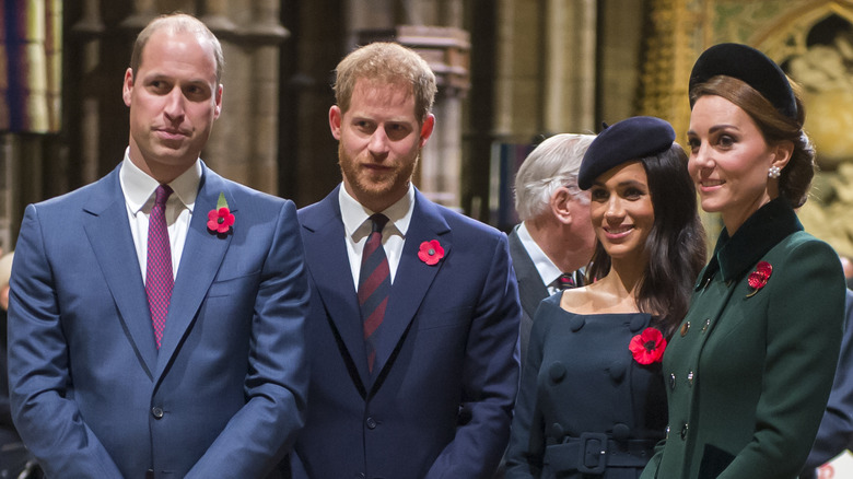 Prince William, Prince Harry, Meghan Markle, and Kate Middleton posing while wearing poppies