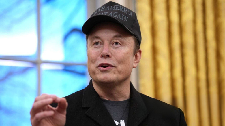 Elon Musk speaking while wearing a black MAGA hat