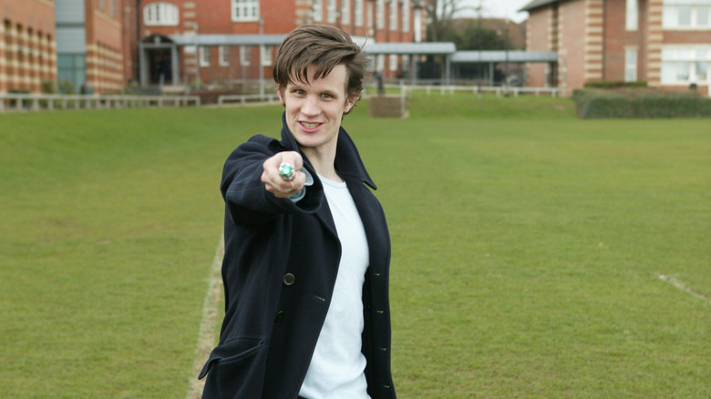 Matt Smith standing on a soccer pitch in a trench coat holding a sonic screwdriver from Doctor Who