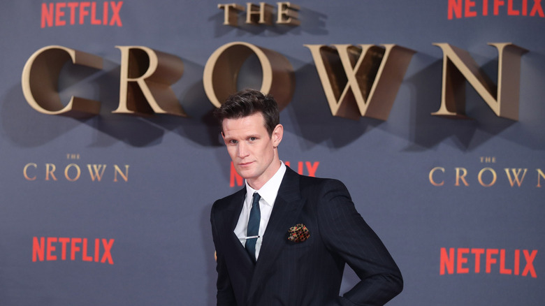Matt Smith wearing a black suit and tie with a patterned handkerchief at a red carpet event for The Crown