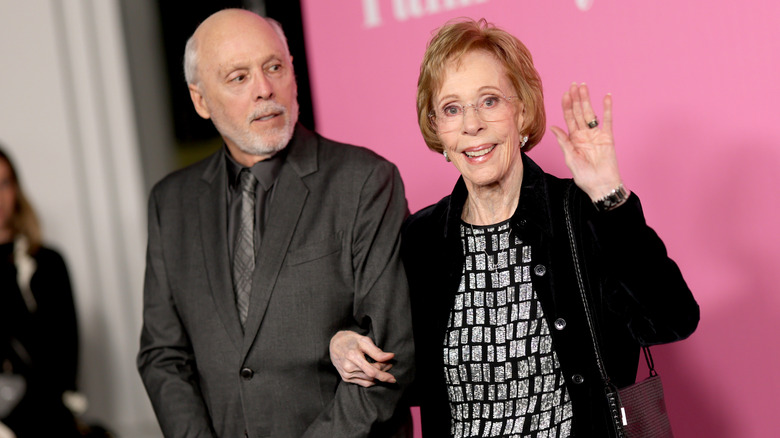 Carol Burnett waves while walking arm-in-arm with Brian Miller in 2026.