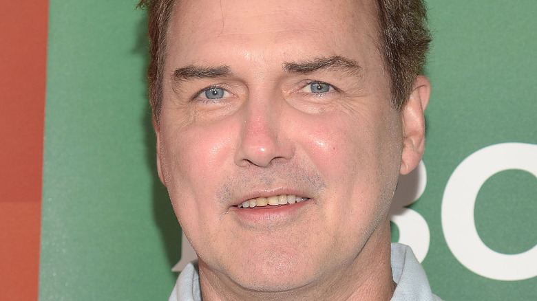 Norm MacDonald smiles in front of a green background