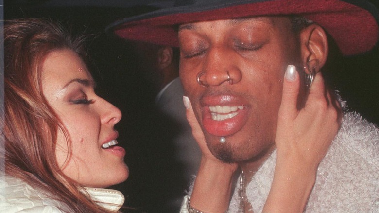 Dennis Rodman wearing a hat, Carmen Electra holding onto his face affectionately