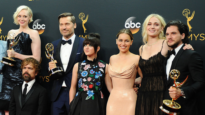 The cast of Game of Thrones in formal suits and gowns while holding Emmys on the red carpet
