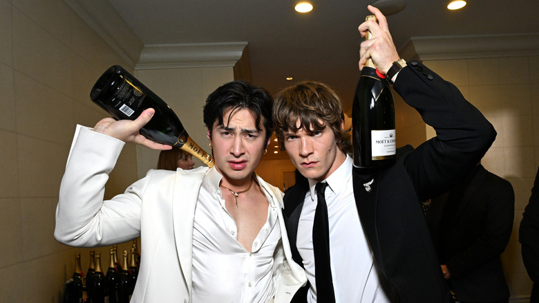 Hudson Williams and Connor Storrie posing in suits with bottles of champagne