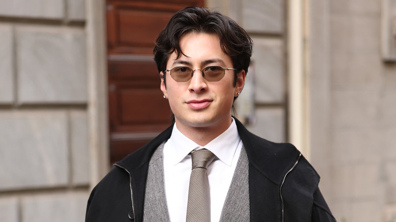 Hudson Williams wearing a black jacket, grey tweed suit, and grey patterned tie