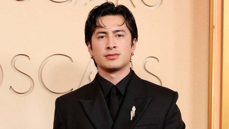 Hudson Williams wearing an all black tailored suit with a gold lapel pin