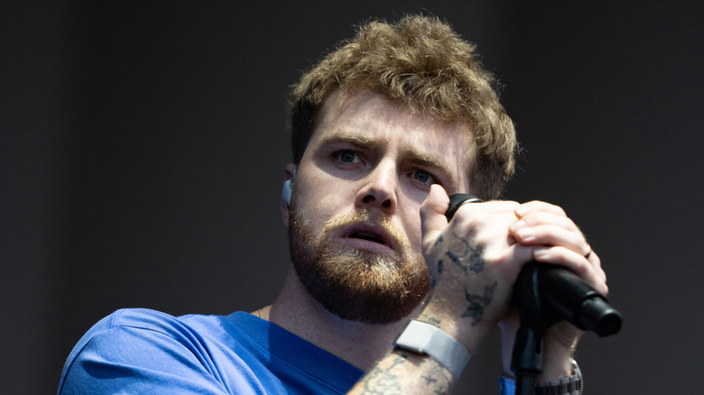 Alex Warren wearing a blue t-short while holding a microphone