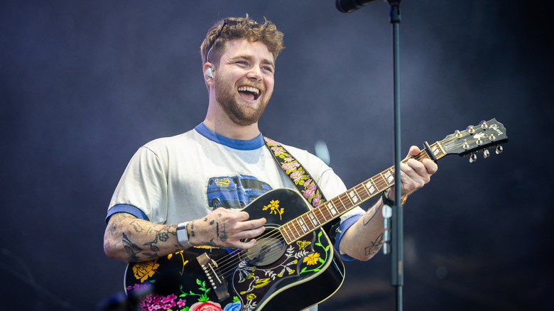 Joyful Alex Warren playing guitar while smiling