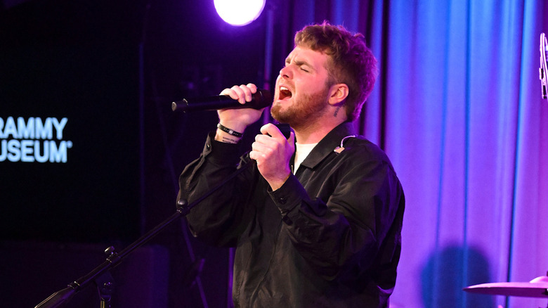 Alex Warren performing onstage in front of purple curtains