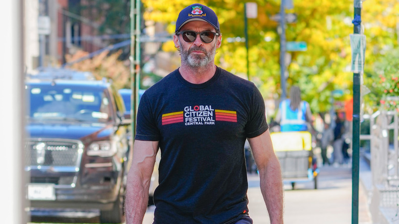 Hugh Jackman walks down street in t-shirt, cap, and sunglasses