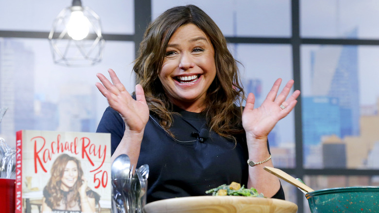 Rachael Ray laughing and holding her hands up during a culinary demonstration