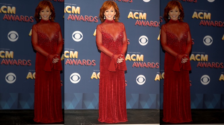 Reba McEntire posing in a red velvet dress at the 2018 ACM Awards