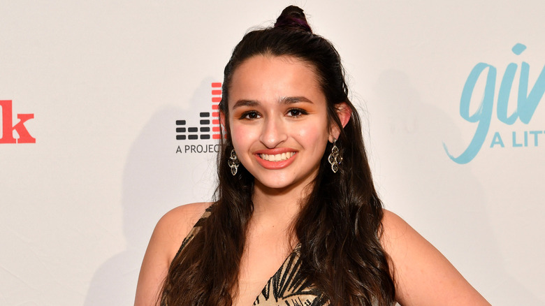 Jazz Jennings, wearing a half bun and full makeup, displaying a radiant smile.