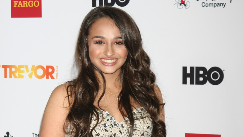 Jazz Jennings, sporting wavy hair and full makeup, smiling on the red carpet.