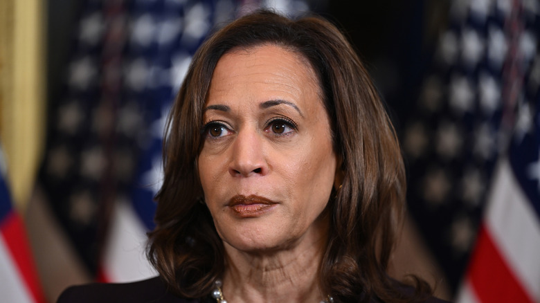 Kamala Harris speaking to reporters in front of flags at the Eisenhower Executive Office Building