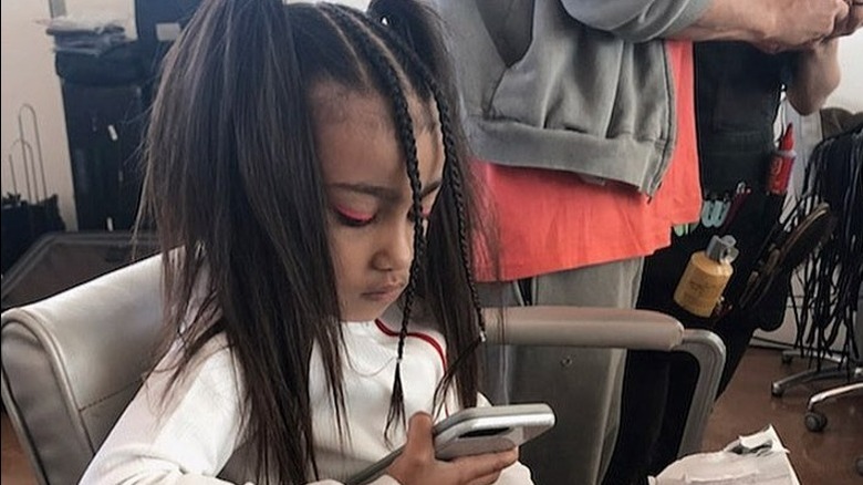 North West with pink eyeliner, looking down at phone