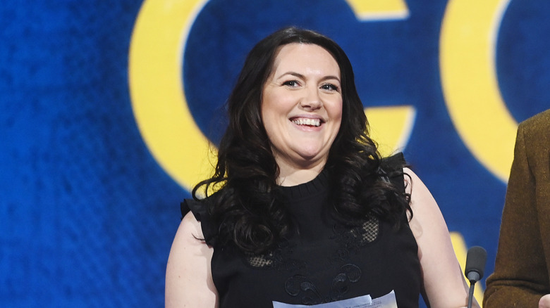 Katy Wix smiling wearing a black sleeveless dress with mesh inlay