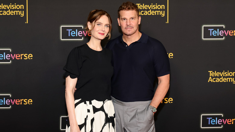 David Boreanaz posing with his arm around Emily Deschanel, with a hand in his pocket.
