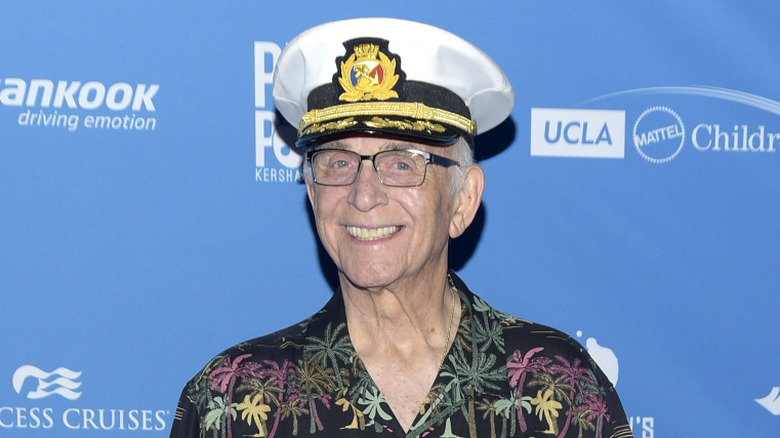 Gavin MacLeod posing on step-and-repeat in a captain's hat