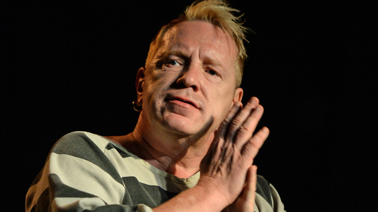 Johnny Rotten, in a prison style shirt, hands clasped