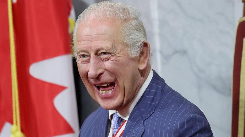 King Charles laughing while photographed in front of a Canadian flag