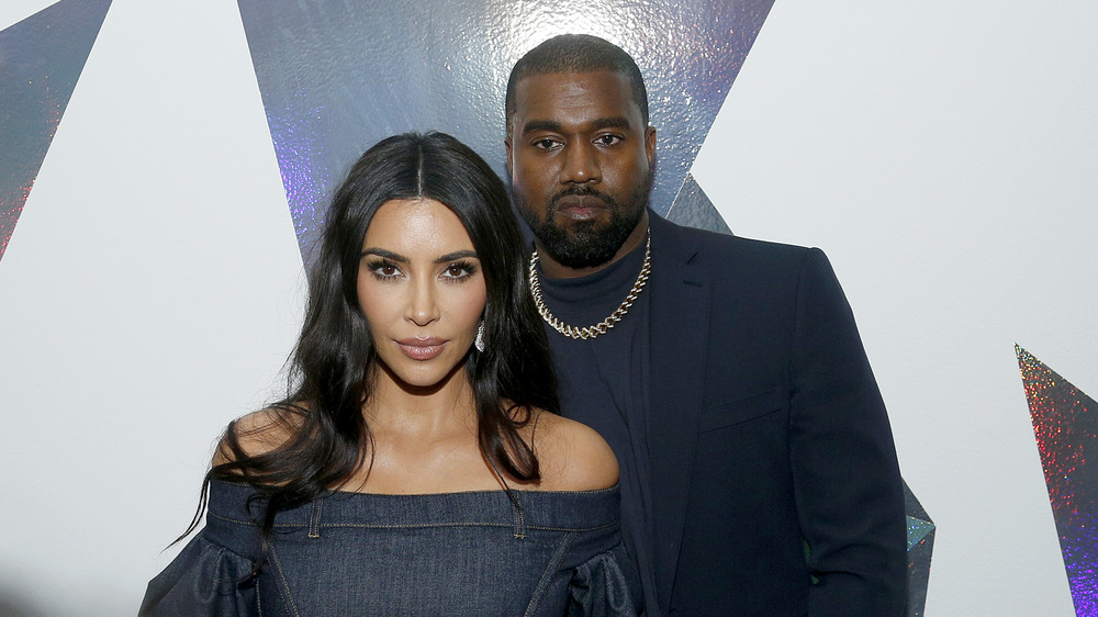Kim Kardashian posing in front of Kanye West, both with serious expressions